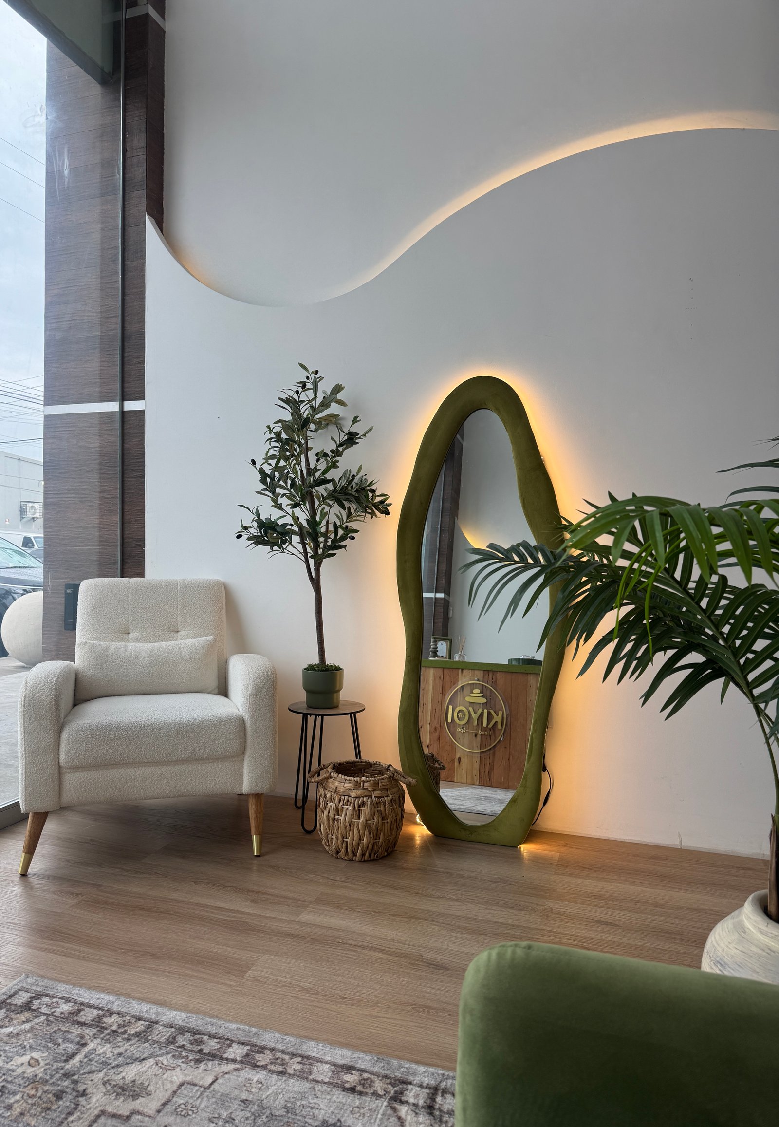 Lobby KIYOI con espejo orgánico iluminado, sillón blanco y plantas naturales